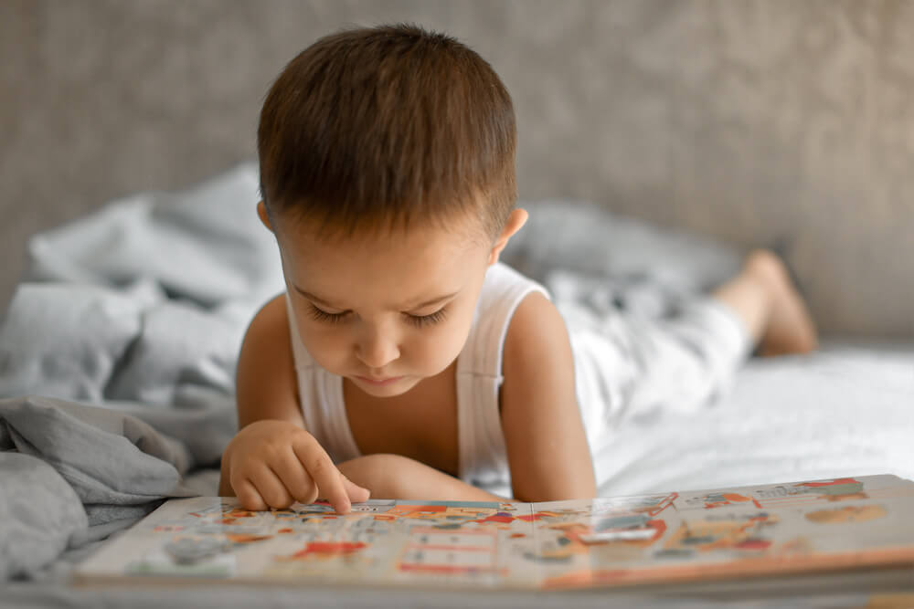 Criança de 2 a 3 anos olhando figuras em um livro, atividade de estímulo à linguagem