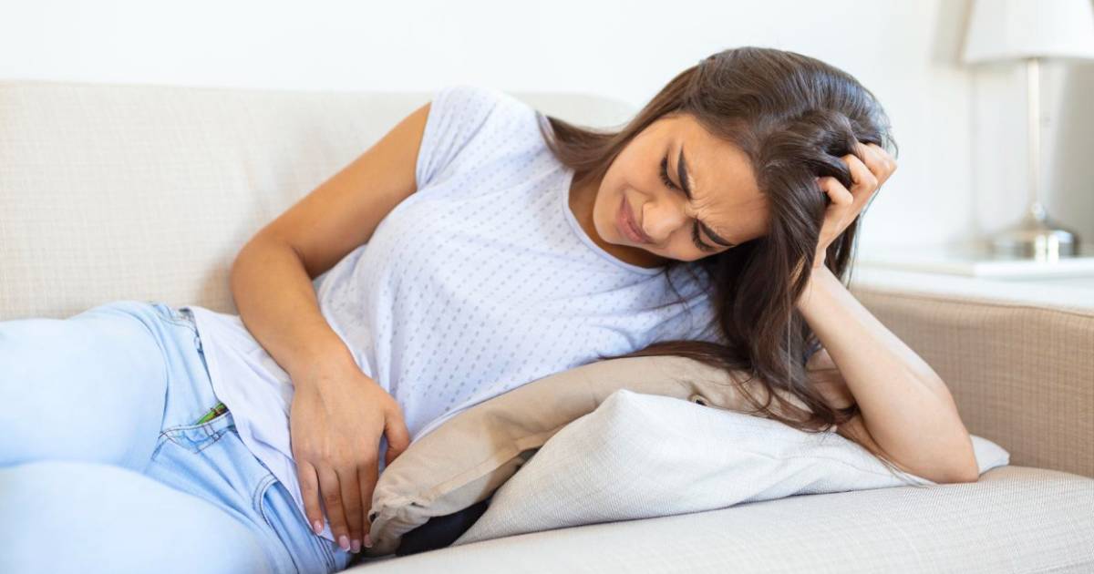 Mulher com dor abdominal intensa por cólica menstrual, deitada com as mãos sobre o ventre