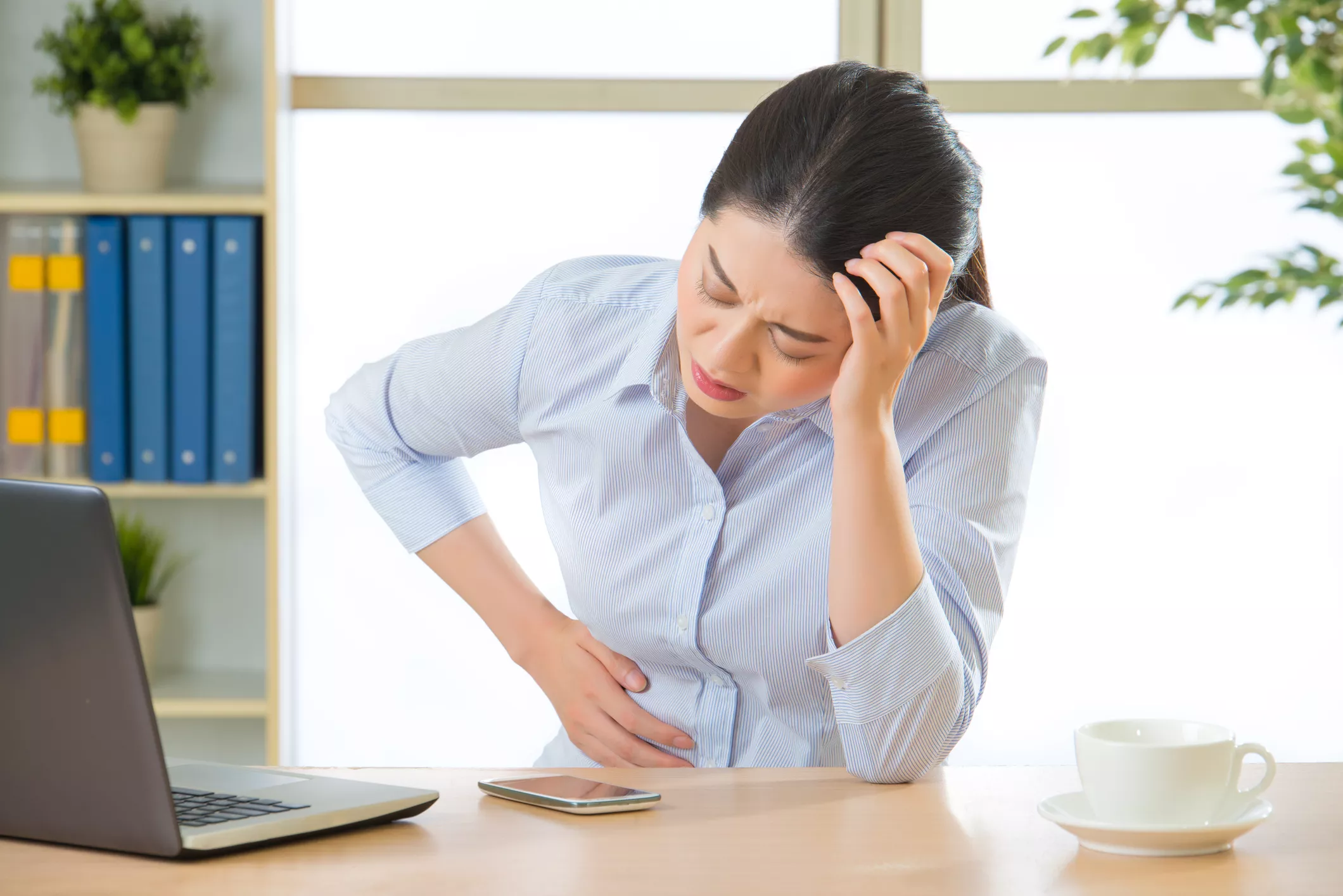 Mulher no ambiente de trabalho, sentada à mesa com a mão na cabeça, em desconforto